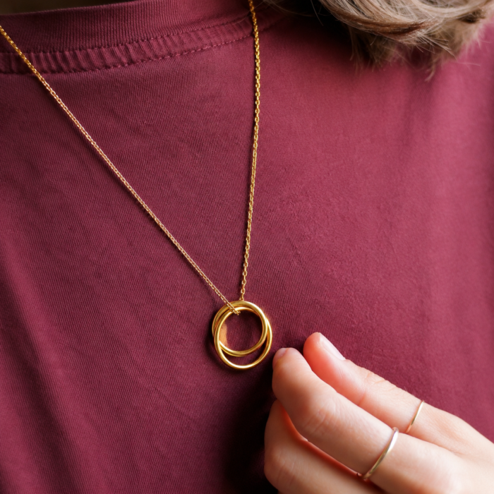 Femme portant un collier pendentif double anneaux entrelacés en or vermeil.