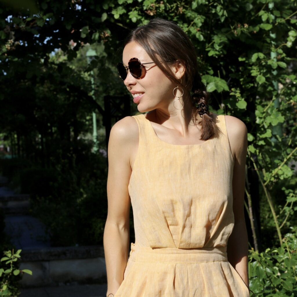 Une femme brune souriante qui porte une combinaison jaune et une paire de boucles d'oreilles pendantes en or